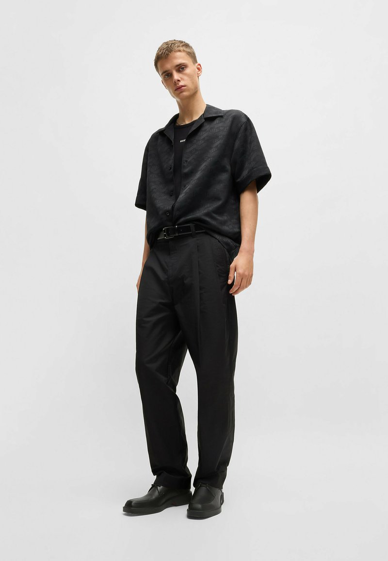 Camisetta nera a maniche corte con un motivo sottile, abbinata a pantaloni larghi neri e scarpe nere. I capi presentano una vestibilità comoda e una texture morbida.