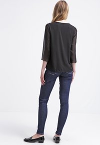 Czarna półprzezroczysta bluzka z rękawami o długości trzech czwartej, gładka tekstura, w połączeniu z ciemnoniebieskimi rurkami i czarnymi balerinami. Widoczne detale na plecach i rękawach.