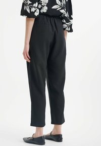 Zwarte, relaxte broek met een elastische tailleband, met een soepele textuur en korte lengte, gecombineerd met zwarte platte schoenen.