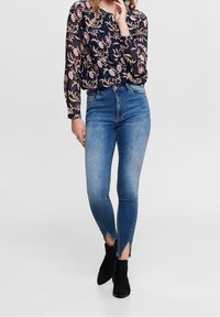 Maglietta floreale blu navy a maniche lunghe con jeans skinny blu a vita alta aderenti con orli a spacco, abbinata a stivali neri alla caviglia.