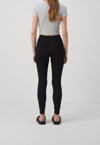 Leggings noirs avec une taille haute et une texture lisse et extensible, associés à un t-shirt gris court et des sandales noires.