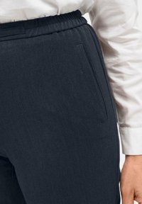 Donkerblauwe, gestructureerde broek met een elastische tailleband, voorzien van een zijzak, gecombineerd met een witte blouse met lange mouwen.