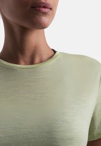 Camisa de manga corta verde claro con una textura suave y aterciopelada. Escote redondo y un sutil brillo, que muestra parte del cuello y la cara.