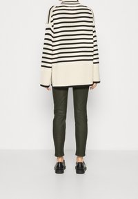 Sweter w paski w kolorze czarnym i kremowym, luźny krój, zestawiony z dopasowanymi zielonymi spodniami i czarnymi butami; gładka tekstura i długie rękawy.