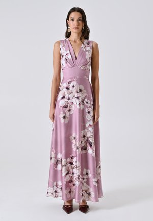Donna che indossa un vestito maxi floreale rosa senza maniche con scollatura a V profonda e scarpe burdeos a punta su uno sfondo neutro.