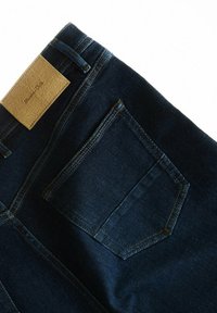 Mörkblå jeans av denim, med kontrasterande sömmar, en rektangulär bakficka och en beige läderetikett på midjebandet.