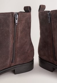 Pair of brown suede ankle boots with side zippers and low black heels on a plain background.