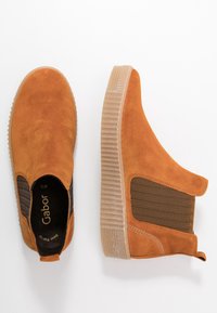 Para krótkich, beżowych zamszowych botków wsuwanych na nogawce z ryflowanymi beżowymi platformami i elastycznymi panelami bocznymi na białym tle.