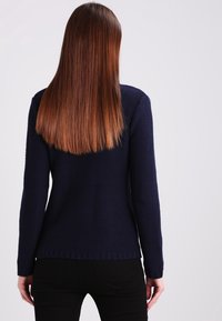 Dunkelblauer Strickpullover mit langen Ärmeln, strukturiertem Stoff und gewelltem Saum. Die Rückansicht zeigt ein tailliertes Design mit gerippten Bündchen.