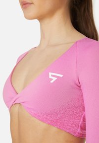 Roza atletska majica s kratkim rukavima, ki ima zasukano sprednje oblikovanje in bel logotip na prsih. Gladka tekstura, prilegajoča oblika.