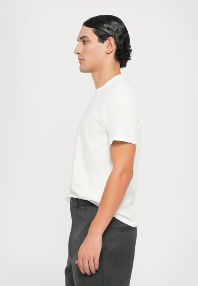 Hvit t-skjorte med korte ermer og rund hals, kombinert med mørke grå bukser. Glatt stoff med en klassisk passform og minimalistisk design.
