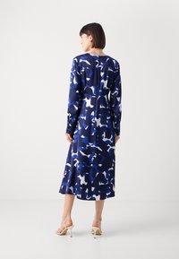 Ρευστό μίντι φόρεμα σε ναυτικές αποχρώσεις με λευκό αφηρημένο σχέδιο. Μακριά μανίκια, κουμπωτές μανσέτες και διακριτική λεπτομέρεια με φερμουάρ στην πλάτη. Λείο ύφασμα.