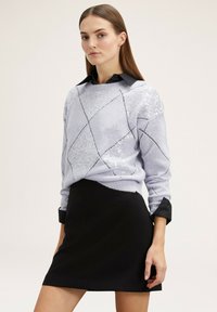 Pullover di colore lilla chiaro con accenti di paillettes e texture a motivo diamante. Abbinato a una minigonna nera e una camicia nera con colletto sotto.