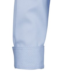 Helle blaue Langarmbluse mit einem gemusterten Manschette, die nach oben gefaltet ist und den detaillierten strukturierten Stoff an der Manschette zeigt.