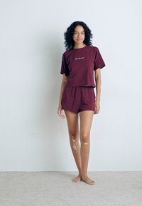Bordeaux katoenen shorts en bijpassende cropped t-shirt set. T-shirt heeft een minimalistisch wit logo. Soepele textuur met een relaxte fit.