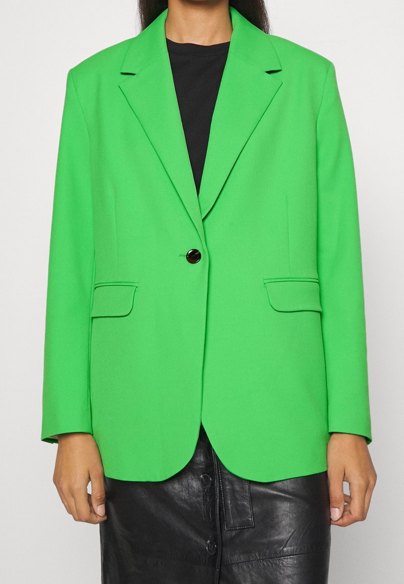 Blazer su misura verde brillante con rever a punta, chiusura a un bottone, due tasche frontali, design strutturato e texture liscia.