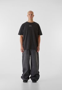 Př oversized černé tričko s nápisem "LOST YOUTH", kombinované se šedými širokými džínami a černými botami. Hladká látka, minimalistický design.