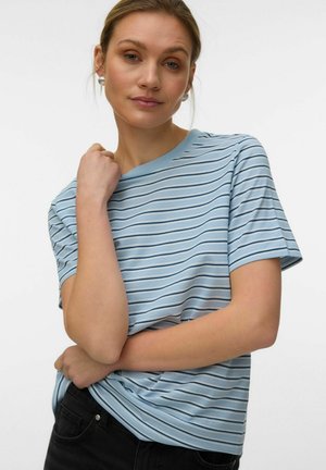 Woman with light brown hair wearing pearl earrings and a blue short-sleeve striped T-shirt, posing with one arm crossed over her waist.