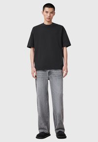 Czarny bawełniany T-shirt z okrągłym dekoltem, zestawiony z jasnoszarymi szerokimi dżinsami. Model nosi czarne buty wsuwane. Prosty design, swobodny krój.