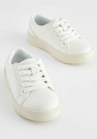 Bílé tenisky s hladkým koženým svrškem, plochými bílými tkaničkami, polstrovaným vnitřkem a béžovou gumovou podrážkou. Klasický nízkoprofilový design.