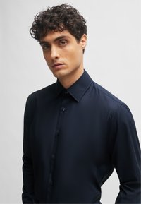 Camicia a maniche lunghe blu navy con collo button-down, texture liscia e bottoni coordinati, dotata di una vestibilità slim e design minimalista.