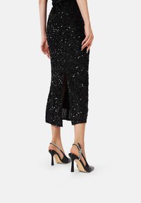 Gonna midi nera con paillettes e spacco posteriori, abbinata a décolleté nere con un accento argento sulla fascia.