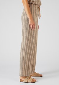 Beige gestreepte wijde pijpenbroek van gestructureerde stof, met een elastische tailleband met een trekkoord, gecombineerd met lichtbruine sandalen.