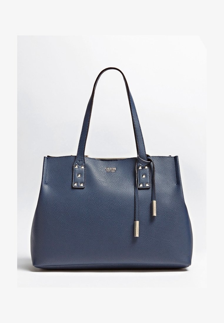Sac fourre-tout en cuir bleu marine avec surface texturée, deux poignées cloutées et un gland décoratif. Dispose d'une fermeture éclair et d'un détail de logo.