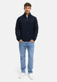 Marinen sweater med en kvart lynlås krave, ribbede manchetter og en glat tekstur, parret med lyseblå jeans og hvide sneakers.