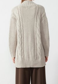 Světle béžový pletený kardigan s detaily kabelkového pletení a texturovanými vzory, s žebrovanými manžetami a lemem, poskytující volný střih.
