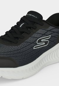Μαύρο και γκρι αθλητικό παπούτσι Skechers με μαύρα κορδόνια, λευκή σόλα και το λογότυπο Skechers "S" στο πλάι.