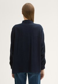 Navyblauw, lichtgewicht shirt met een knoopsluiting bij de manchetten, puntige kraag en een ontspannen pasvorm. Heeft een subtiele verticale textuur. Achteraanzicht weergegeven.