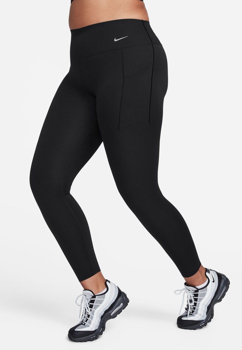 Svarte leggings laget av elastisk stoff har høy midje og to baklommer. Kombinert med svart-hvite treningssko.