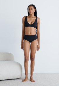 Set di bralette nera e mutandine a vita alta, realizzato in morbido tessuto, con design a scollatura a V e texture liscia e elastica.