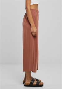 Jupe longue marron en tissu doux, avec une taille élastique. Associée à des sandales noires avec une semelle en liège.