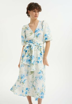 Abito midi floreale in tessuto leggero, con motivi floreali blu su sfondo bianco, scollatura a V, maniche a sbuffo e vita con laccio.