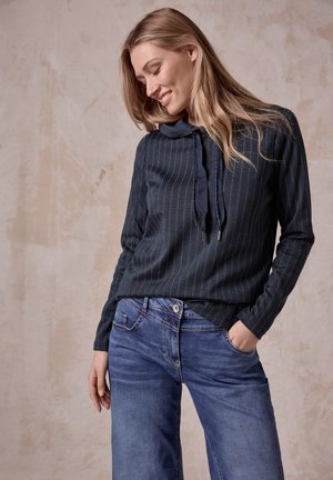 Navy gestreepte lange mouwen top met een koordsluiting bij de nek, gecombineerd met lichtblauwe wijde jeans. Soepele textuur, casual pasvorm en zichtbare zakken.