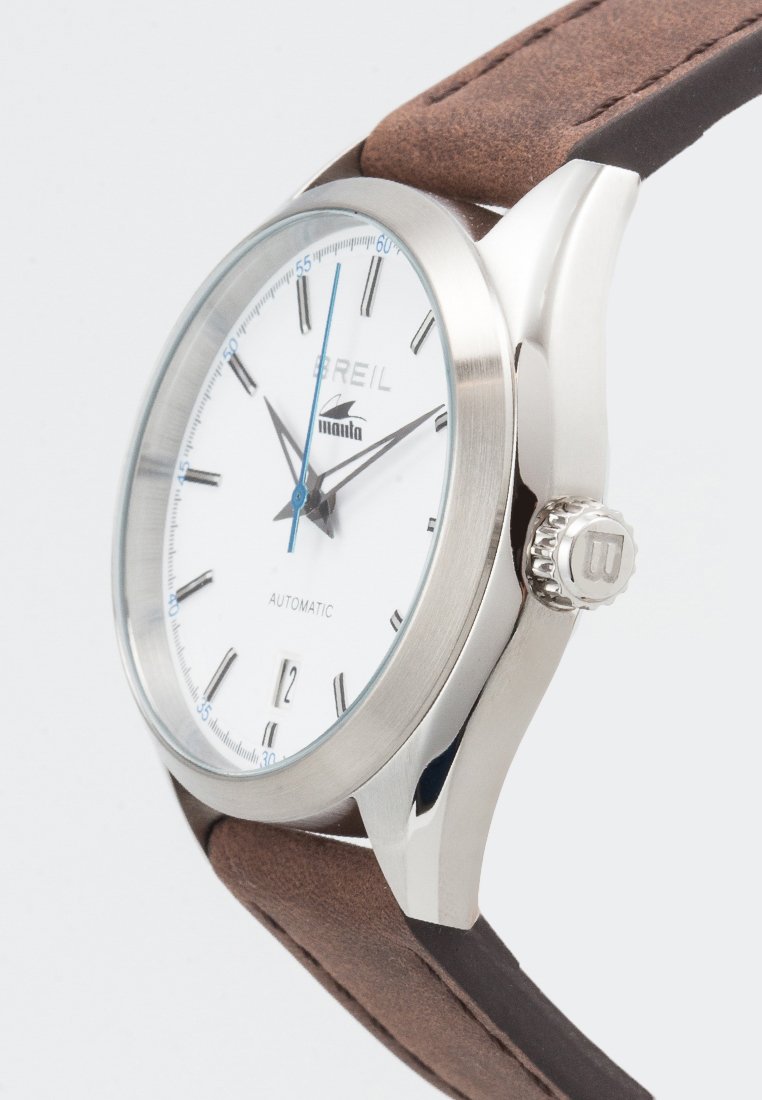 Reloj de acero inoxidable plateado con un dial blanco, agujas azules y una correa de cuero marrón. Incluye movimiento automático y una corona texturizada.