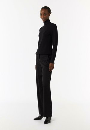 Schwarzer Rollkragenpullover mit langen Ärmeln, kombiniert mit schwarzen, taillierten Hosen. Das Ensemble weist eine elegante Silhouette und eine glatte Textur auf.