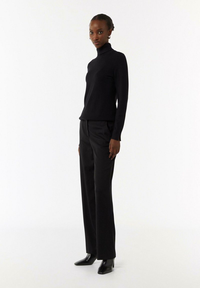 Schwarzer Rollkragenpullover mit langen Ärmeln, kombiniert mit schwarzen, taillierten Hosen. Das Ensemble weist eine elegante Silhouette und eine glatte Textur auf.