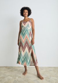 Maxi dress with a chevron pattern in green, peach, and brown. Features spaghetti straps and a thigh-high slit. Made of lightweight fabric.