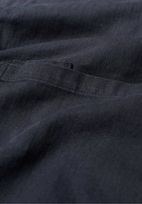 Crni materijal s uzorkom riblje kosti, koji ima glatku teksturu i malu rupu vidljivu u materijalu.