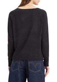 Maglione nero a maglia con un fit rilassato, scollo ampio e polsini e orlo a coste, abbinato a jeans a vita alta con tasche posteriori ben definite.