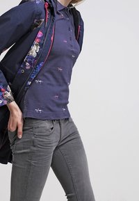 Marinblå polotröja med knappar, med ett diskret blommönster. Kombineras med figurnära grå jeans och en marinblå jacka med blommor.