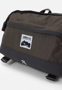Mörkgrön tygväska med svart botten. Har en vit Adidas Adventure-logotyp och texten "7L." Inkluderar justerbar rem och detaljer.