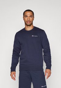 Sweatshirt bleu marine en tissu mélangé de coton. Il présente un col rond, des manches longues, des poignets côtelés et un logo brodé sur la poitrine.