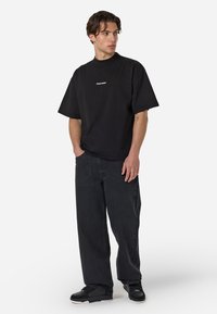 Sort oversized t-shirt i bomuld med runde halsudskæring, parret med løse sorte denimjeans og sorte sneakers. Enkelt logo detalje på skjorten.