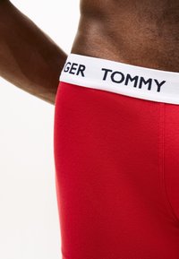 Άνδρας με κόκκινο εσώρουχο Tommy Hilfiger με λευκή ζώνη μέσης που δείχνει το όνομα της επωνυμίας.