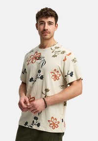 Camiseta de algodón beige con un estampado floral en todo el tejido en naranja, verde y azul marino. Cuello redondo, mangas cortas y un corte relajado.