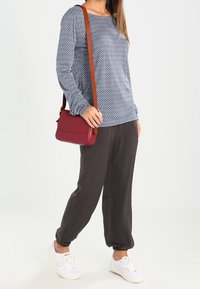 Mörkblå mönstrad långärmad topp, grå joggerbyxor, vita sneakers och en liten röd axelremsväska med brun rem.